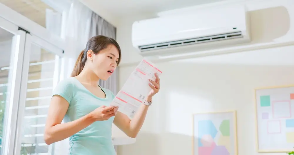 Mulher preocupada segurando conta de luz em ambiente com ar-condicionado.